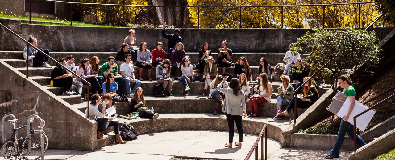 Student sit in an amphitheater as they take notes and raise their hands