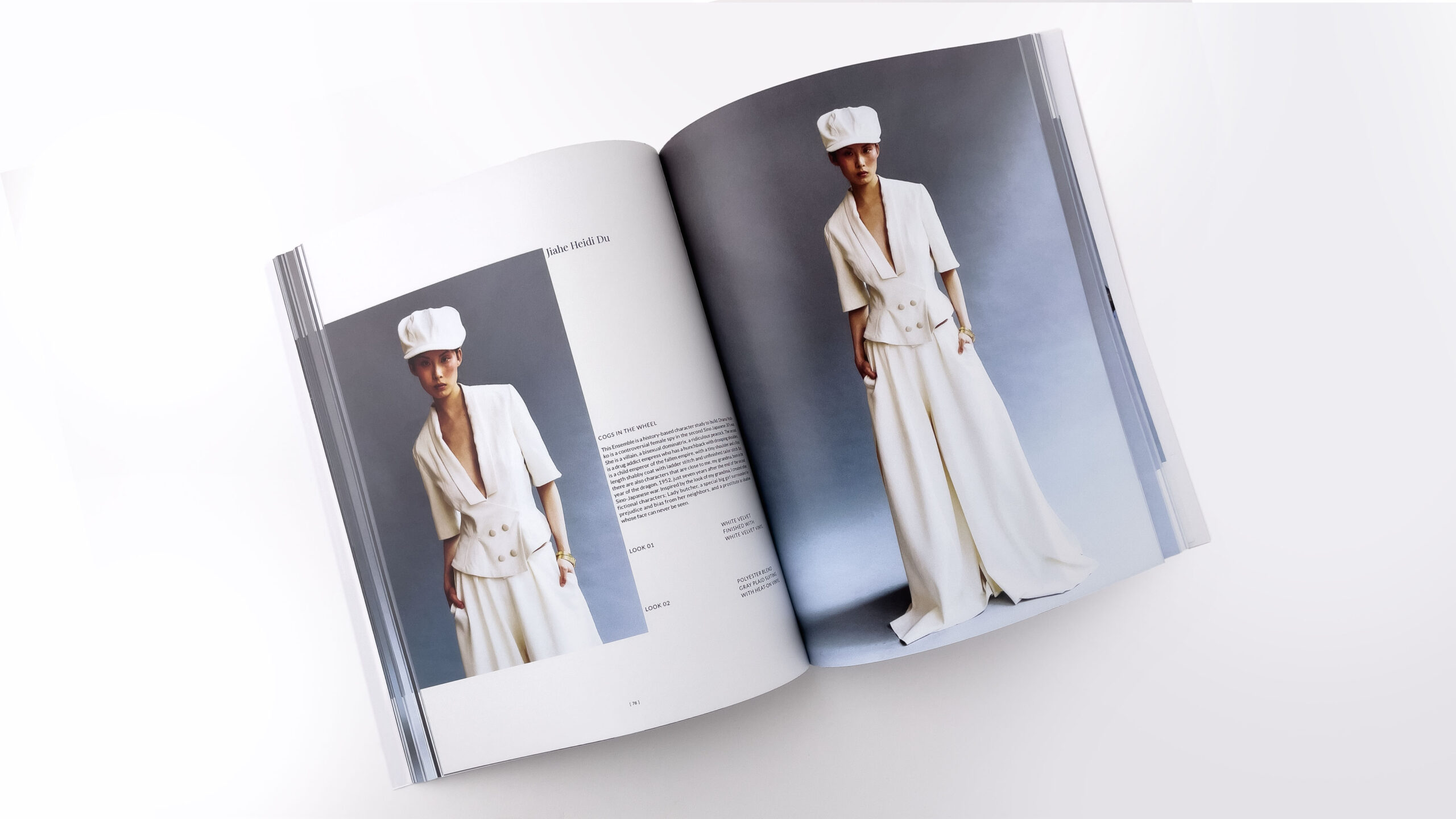 An open fashion lookbook lies on a white surface, displaying a model wearing an all-white tailored outfit photographed against a neutral studio background.