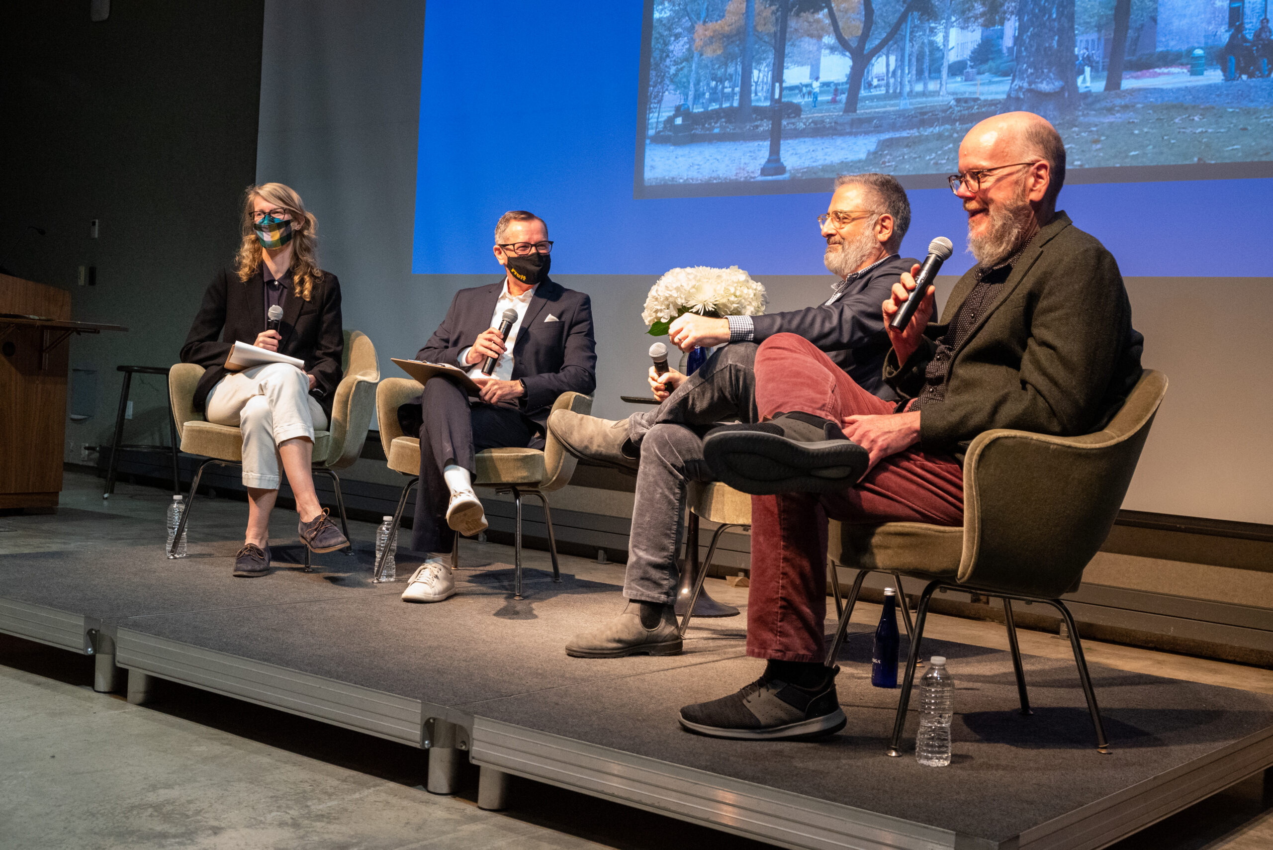 A discussion panel is assembled in front of a projector screen. There are four panelists with the person on the right holding a mic.