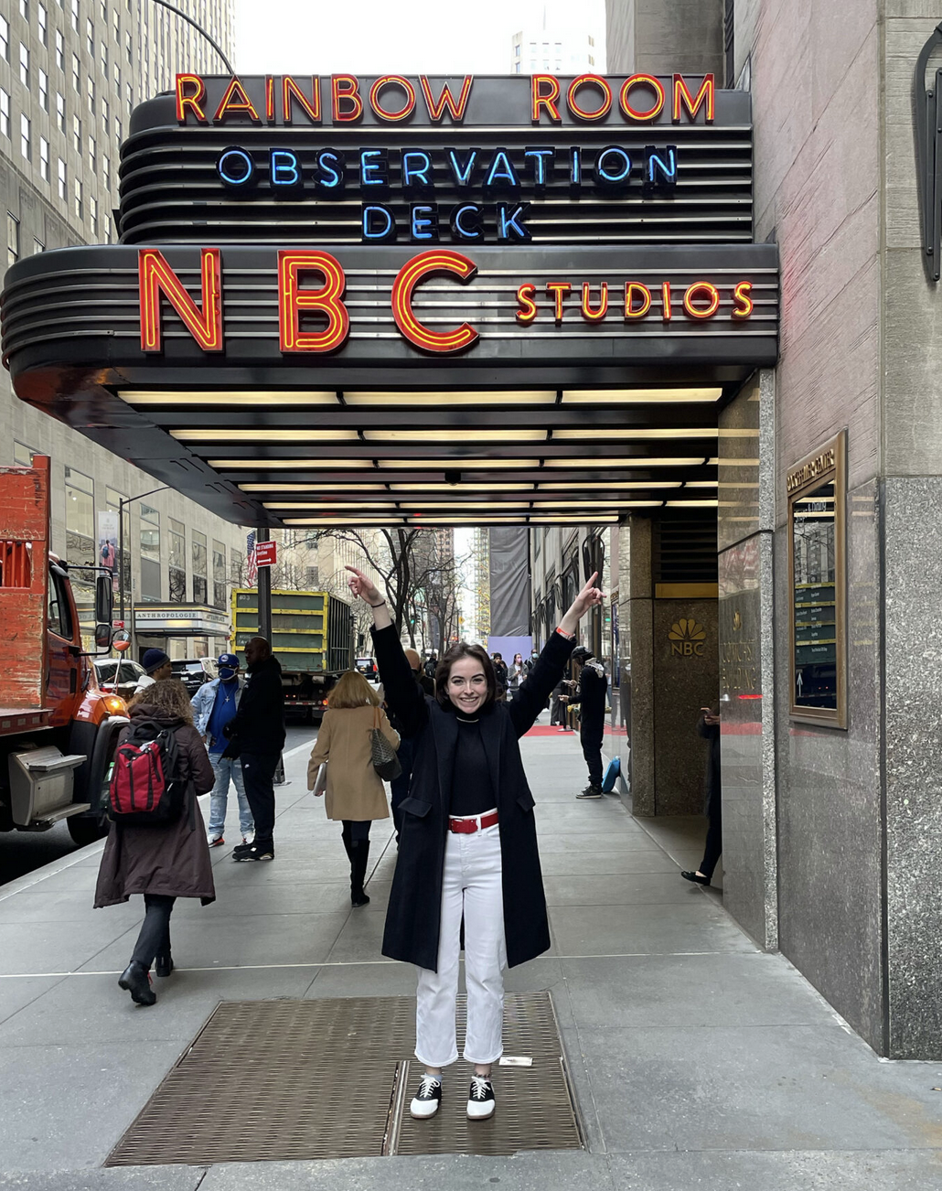 student standing outside nbc studios, arms raised