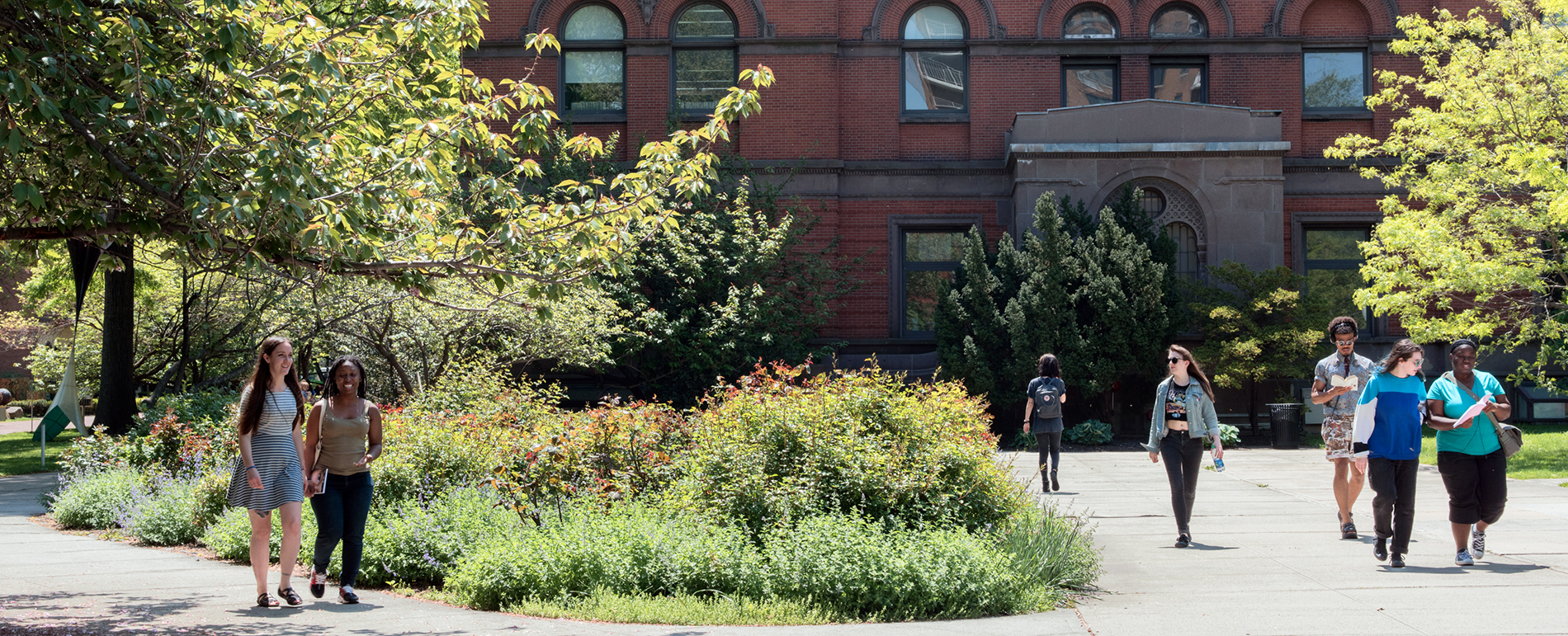 Students walk along a path in front of a red brick building.