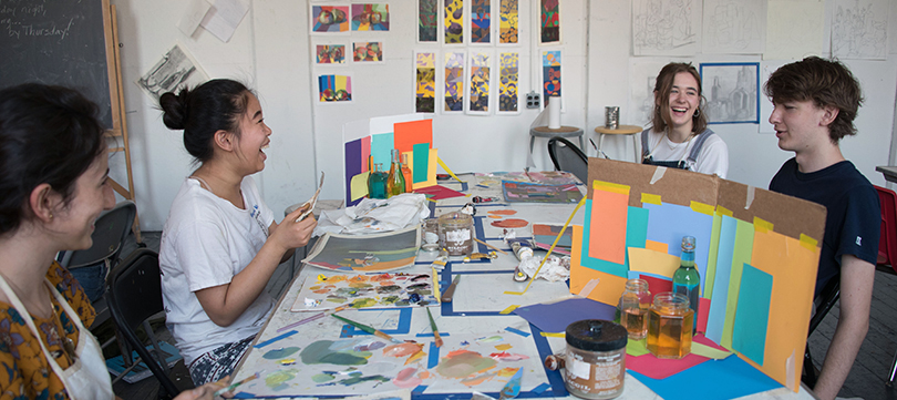 A group of students sit around a table in an art studio.