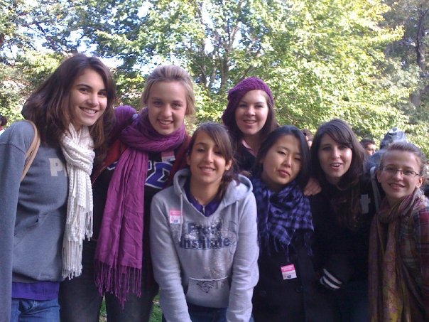 A group of sorority members stands for a group photo with a foliage behind them.
