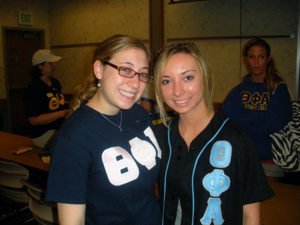 Two sorority members smile for the camera with a dark room behind them.
