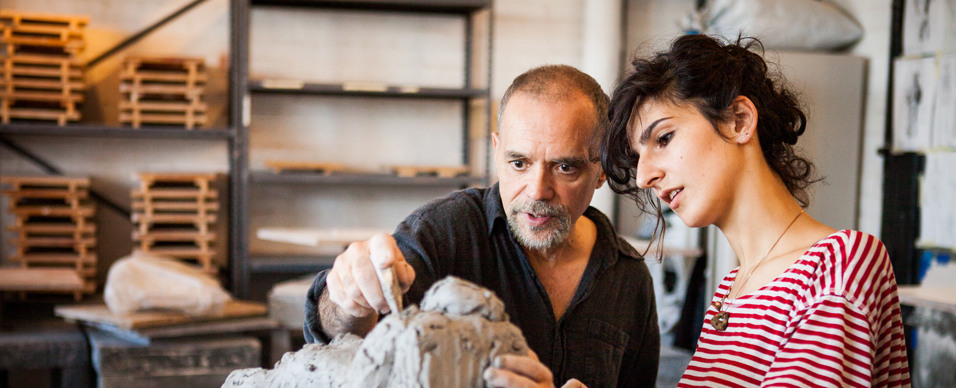 A professor points at an in-progress clay structure, giving feedback to a student.