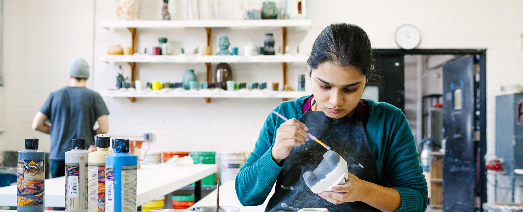 A student paints a clay sculpture inside a kiln studio.