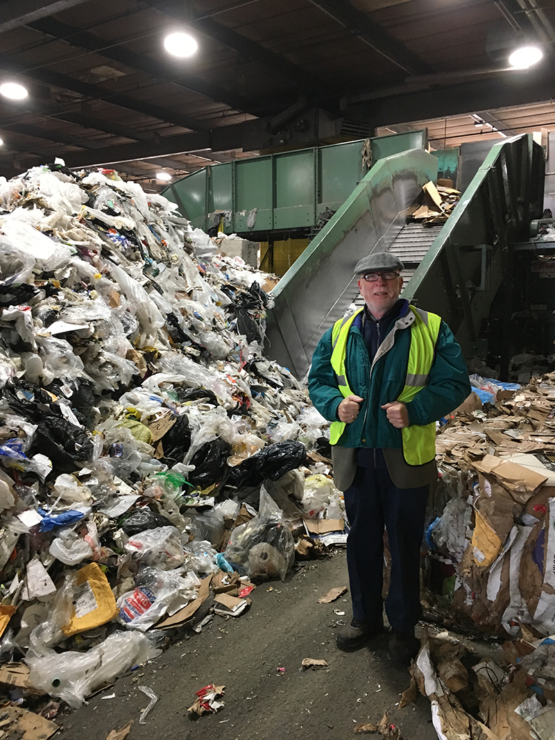 image of a man in a reflective work vest standing next to a garbage truck and a heap of recycleables
