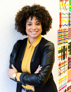 Jazmin Peralta smiles at the camera wearing a black jacket and a yellow shirt.
