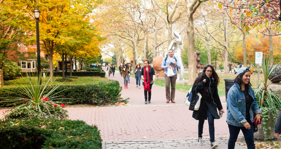 A large group of students walks through a park with sculptures scattered throughout.