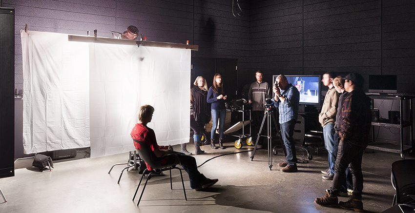 Students receive a lecture in a photography studio with various lighting equipment.