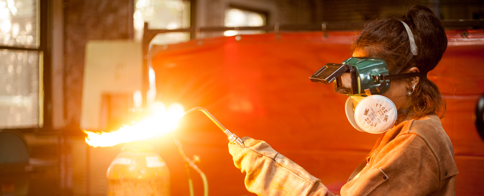 A student welds in a welding room with protective equipment on.