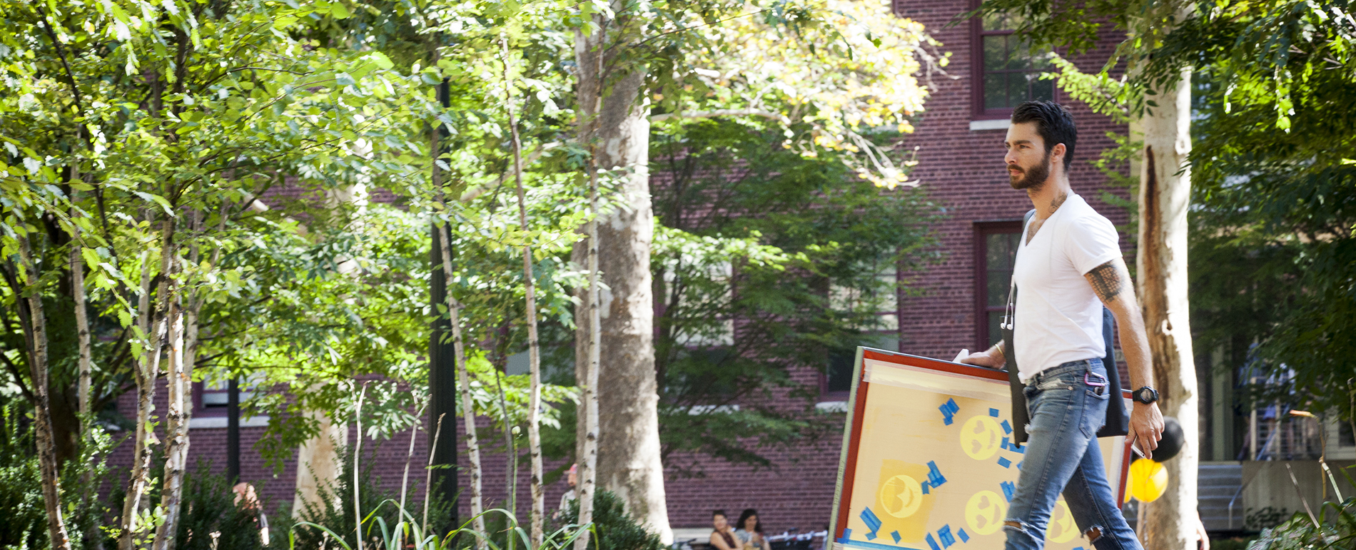 A person walks through a park while carrying a large stencil.