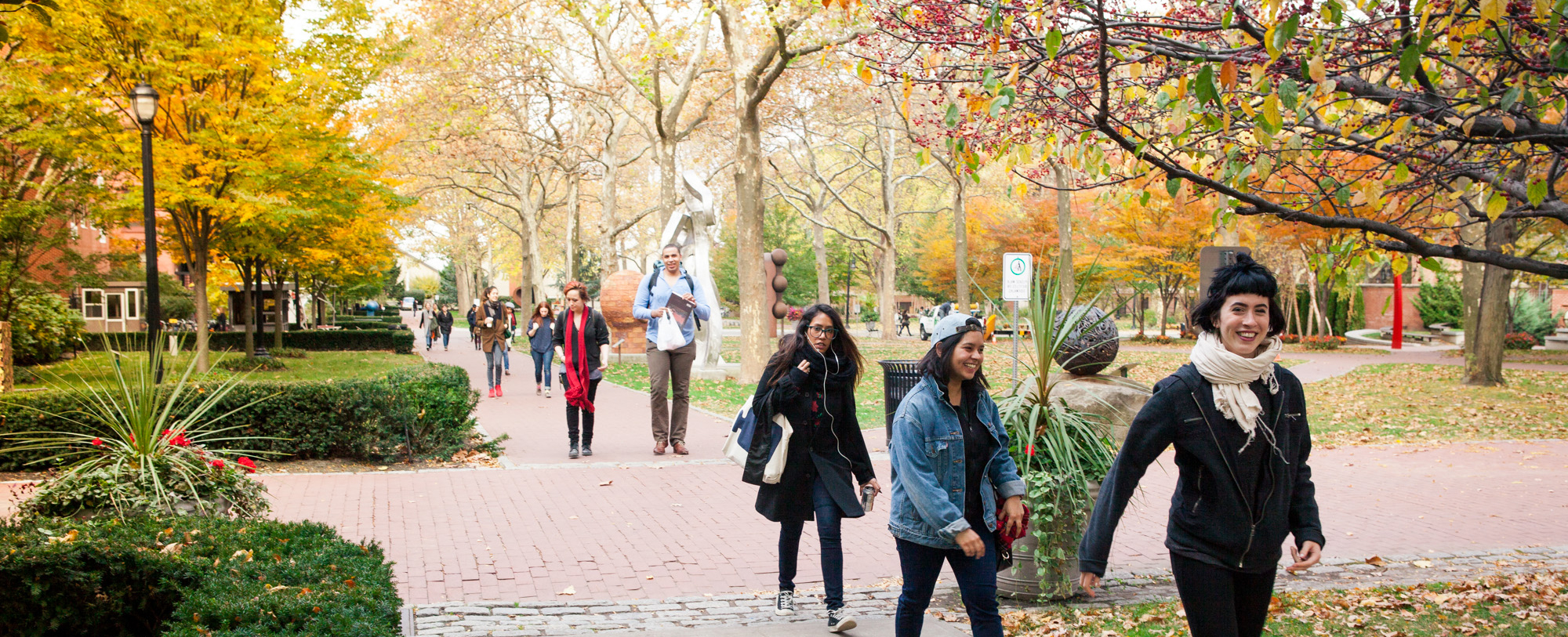 Students walk through a wooded park on red brick path