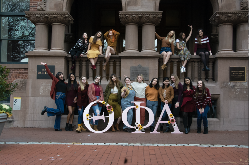 Sorority members stand in group with the huma-size greek letters for Theta Phi Alpha