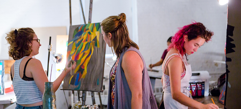 Three people stand and paint in art studio.