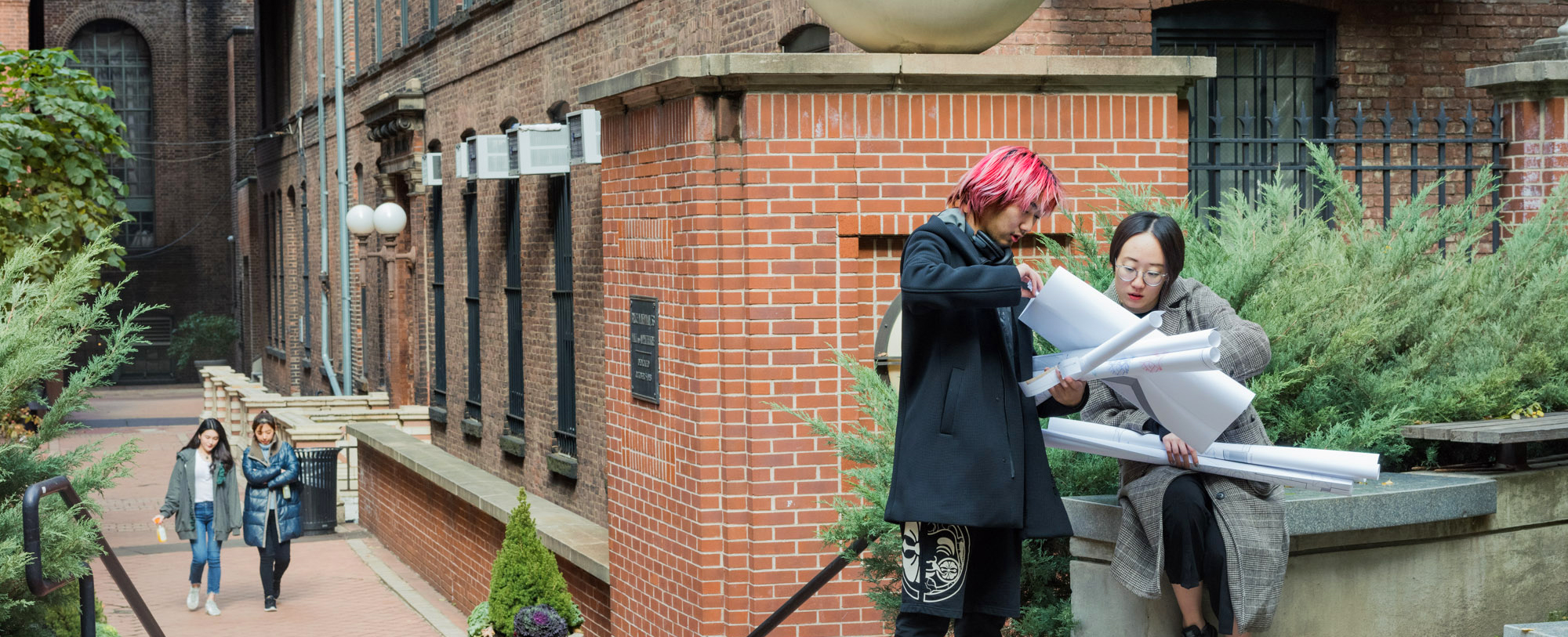 Students look at designs on posters in courtyard with a brick wall