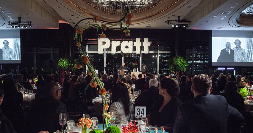 A large crowd sits in front a speaker in a Pratt stage