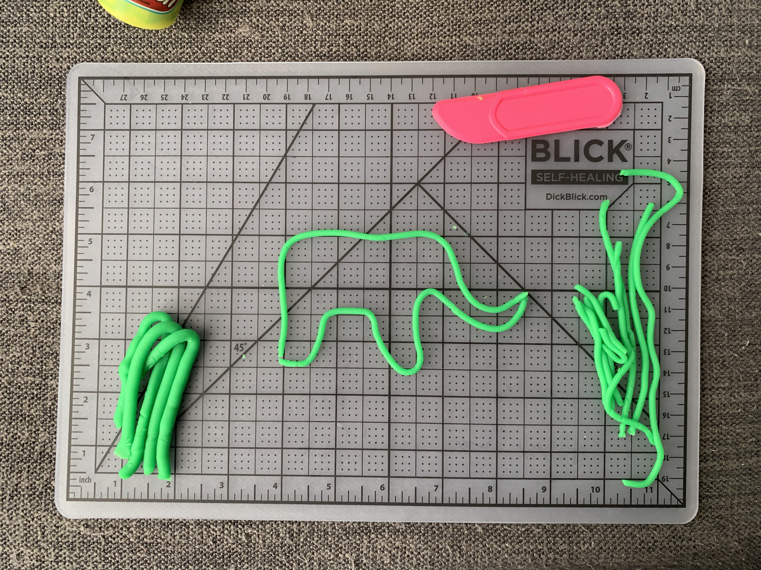 An elephant sketch made of a thin string of neon green play-doh is on top of a grid mat with pieces of neon green play-doh off to the side.