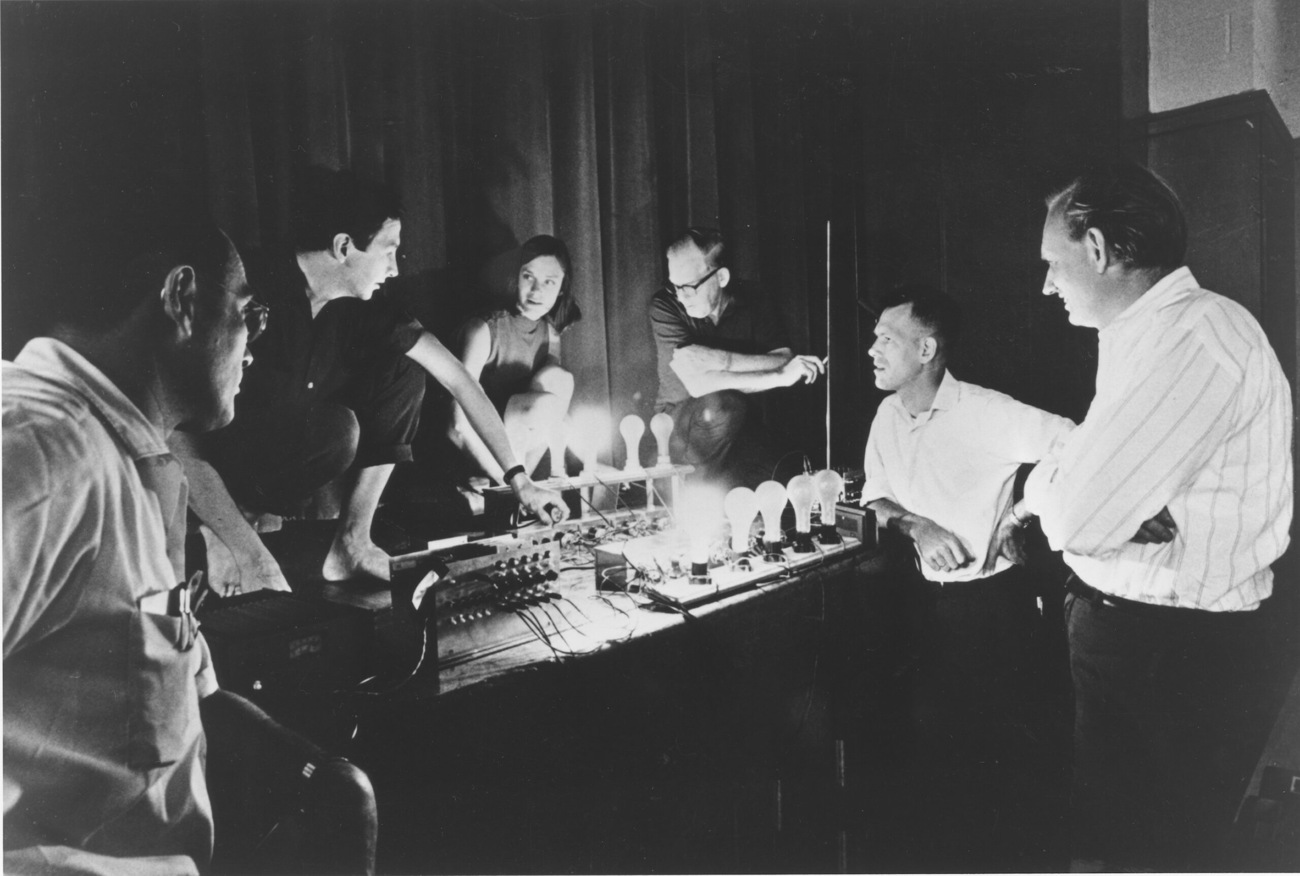 artists stand around a row of variously lit lightbulbs.