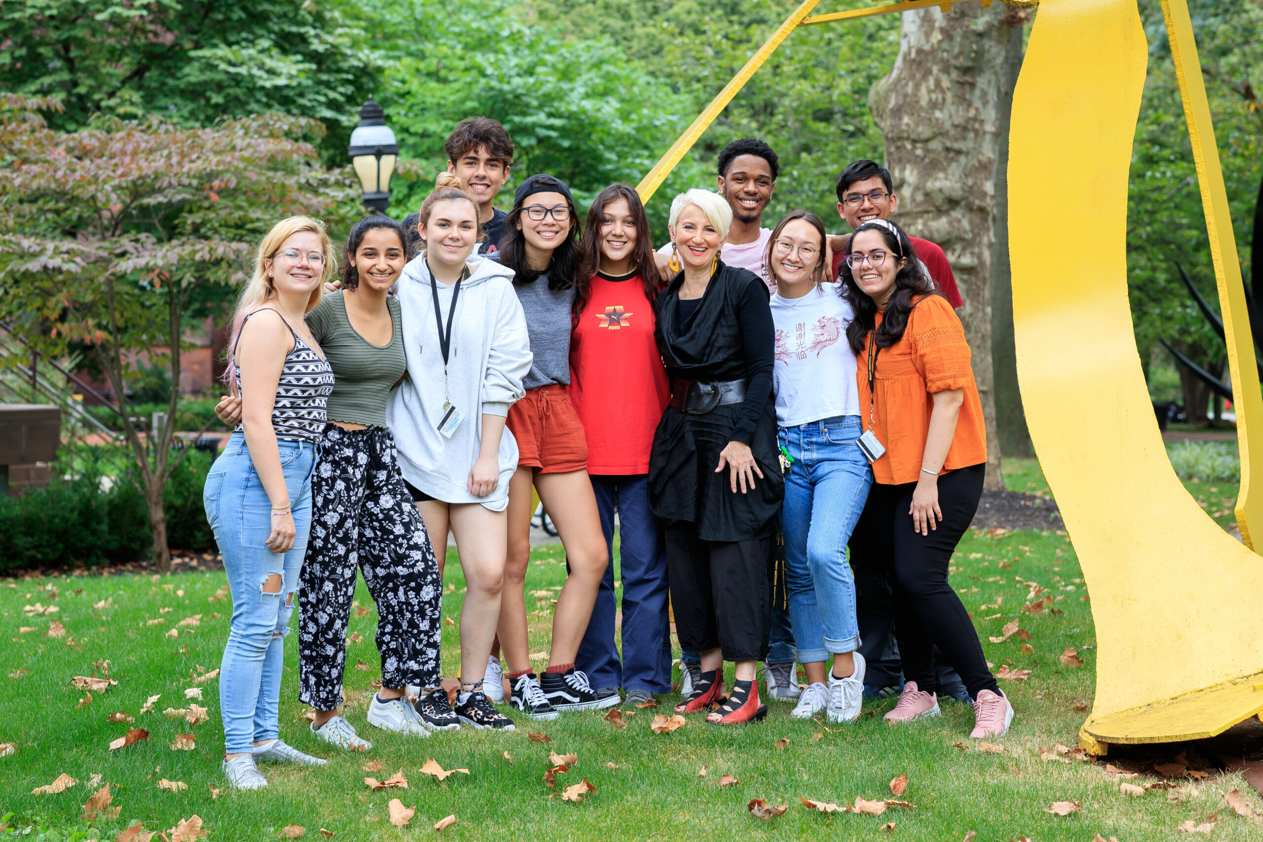 a group of students poses with President Frances Bronet outside on campus with a yellow sculpture behind them.