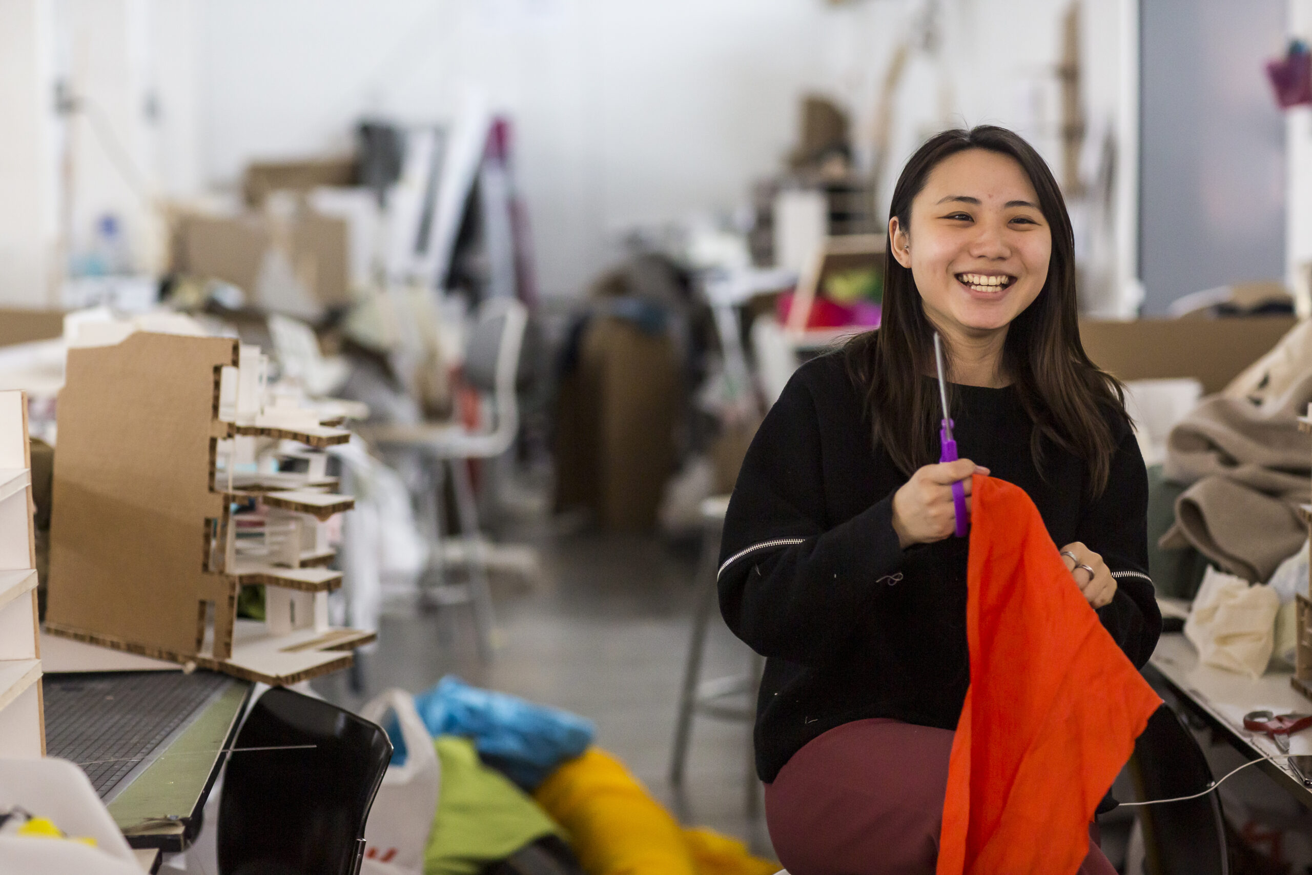 student in fabric workshop, smiling, looms and work behind her in the background