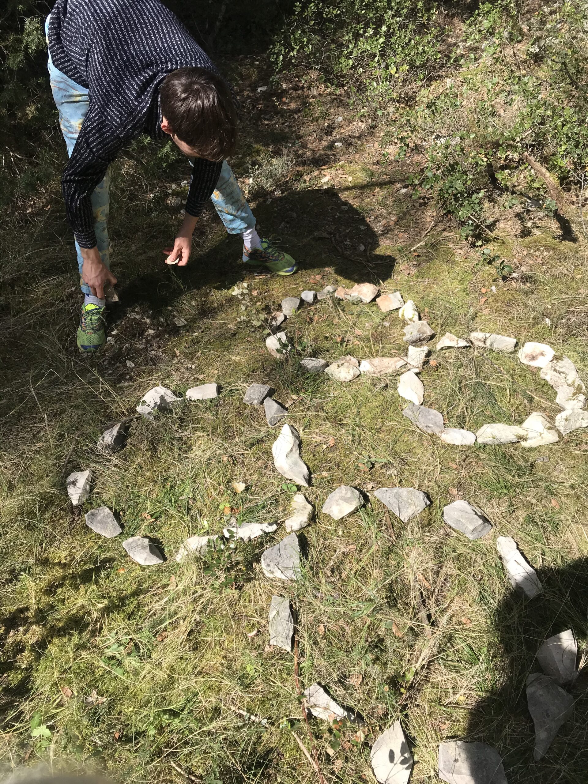 person leans over a collection of stones in two infinity symbols that are side by side in the grass.