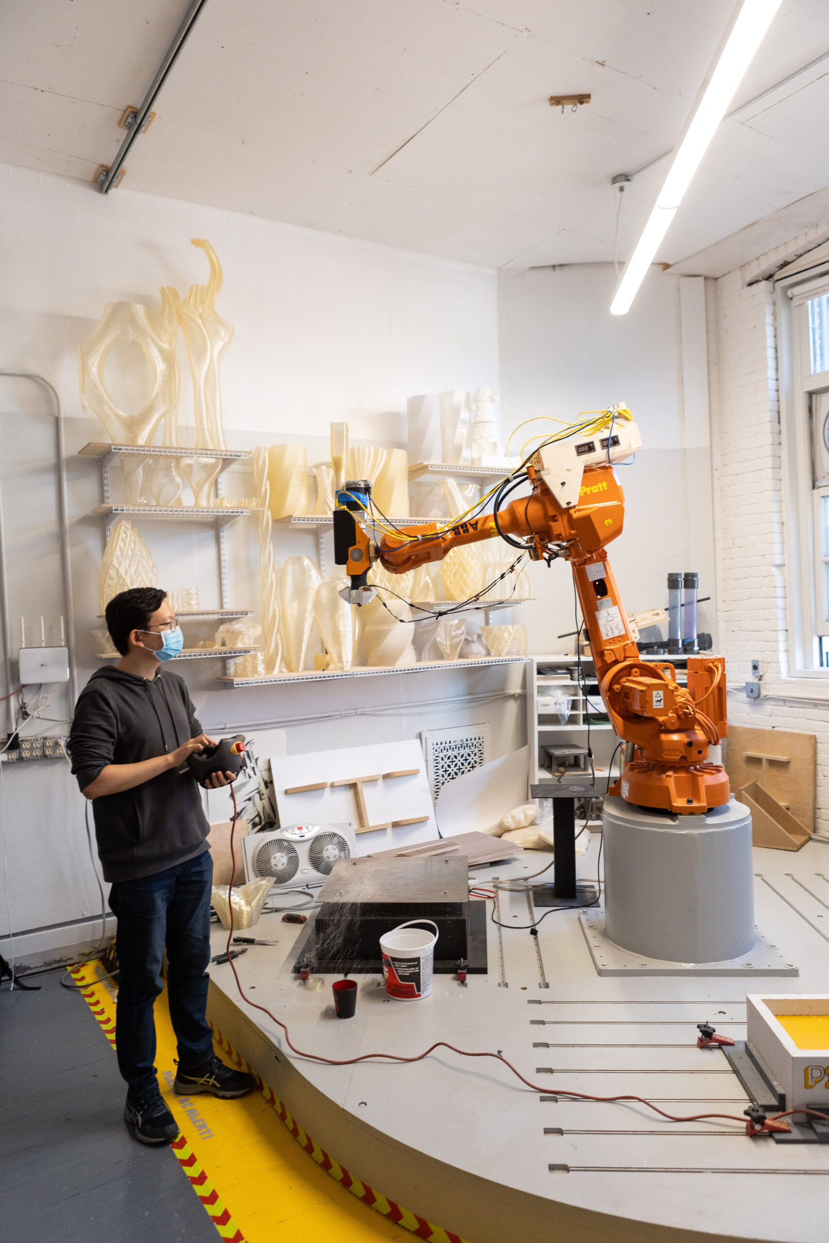 A person stands in a studio next to a large, orange robotic arm