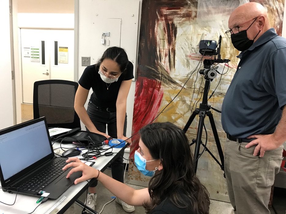 group of researchers standing at a computer with painting behind them.