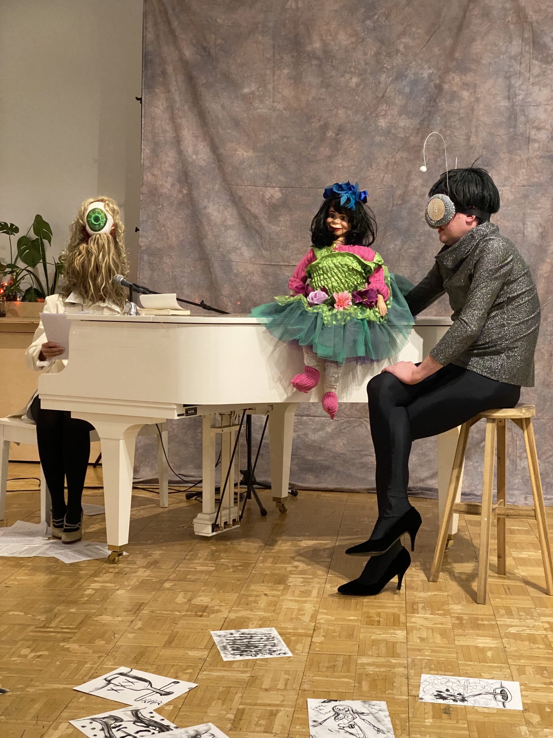 wo performers in costumes with a ventriloquist dummy at a white grand piano