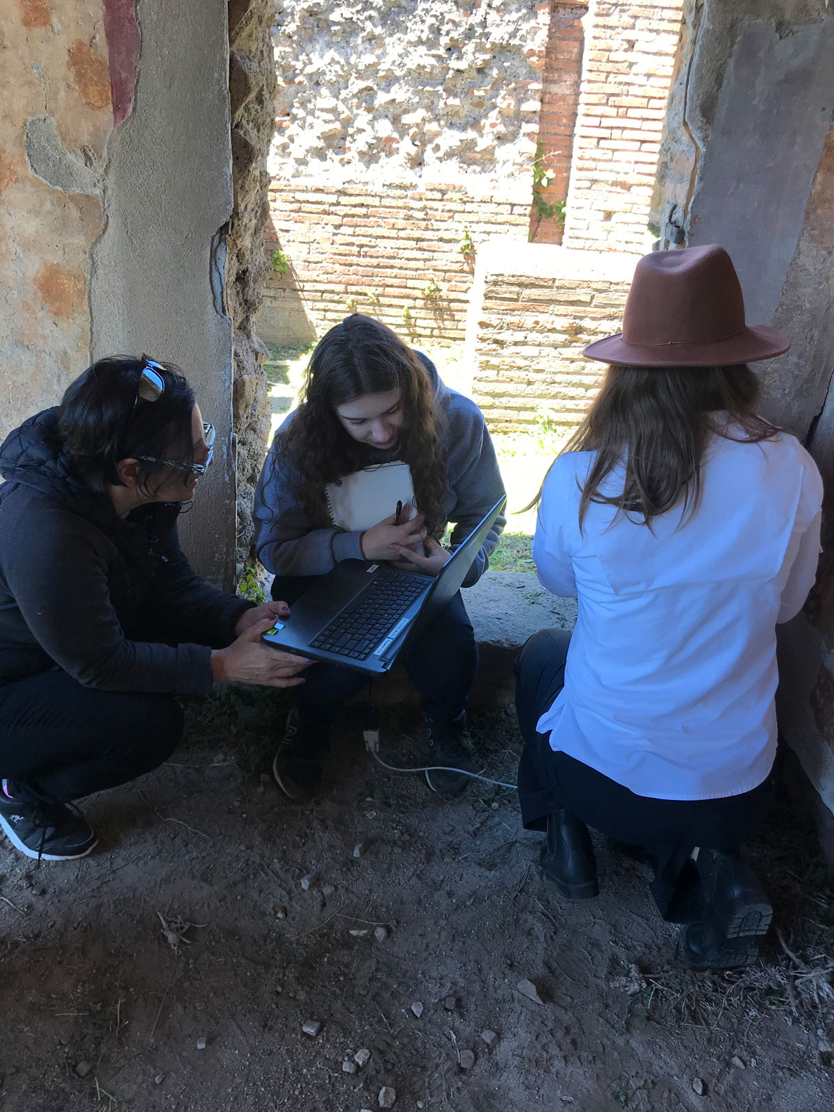 Researchers are crouched next to an ancient wall, looking over data on a laptop
