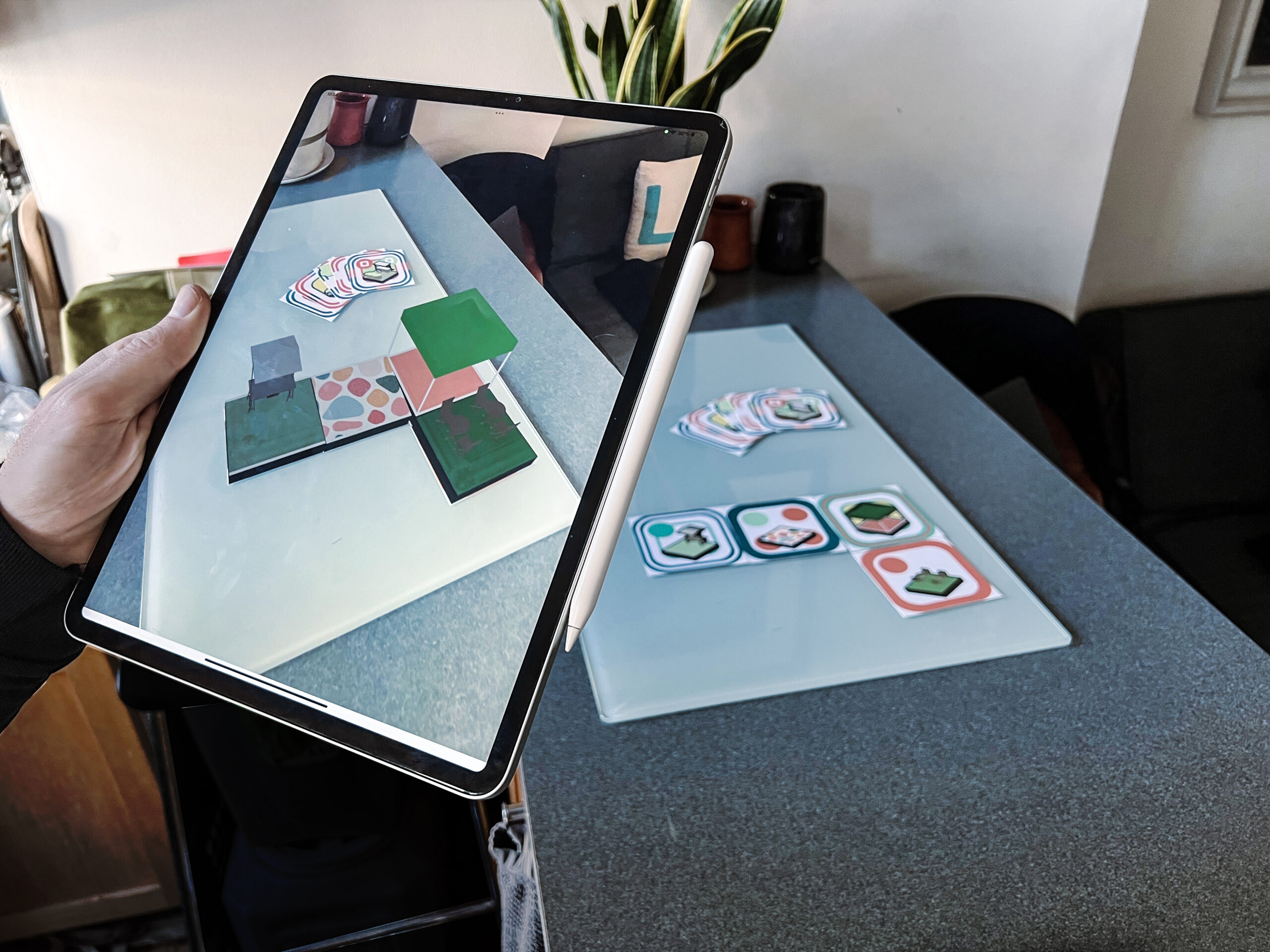 hand holds computer tablet with Kalye program visible on screen and corresponding tiles on the table.