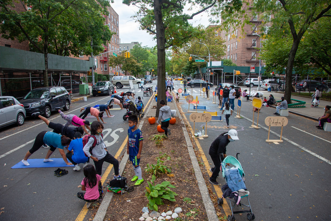 residents doing various activities on the closed street, like adults doing yoga and children standing and playing on the median.
