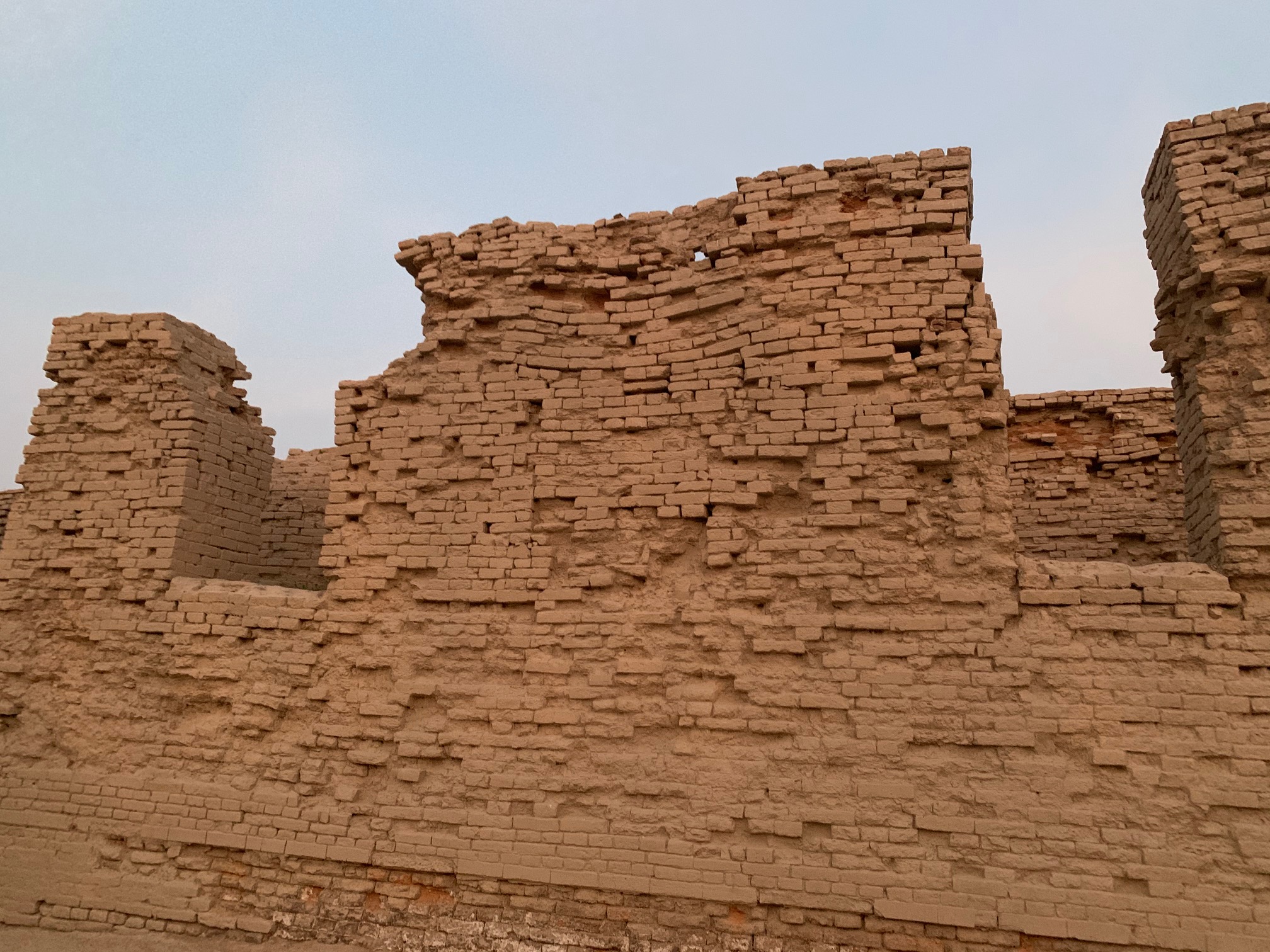 A brick wall located in the archaeological dig site of MohenjoDaro, Pakistan. The wall was likely once a side of a house, though it is partially destroyed now with no roof remaining. Two doorways are visible as large gaps in the wall.