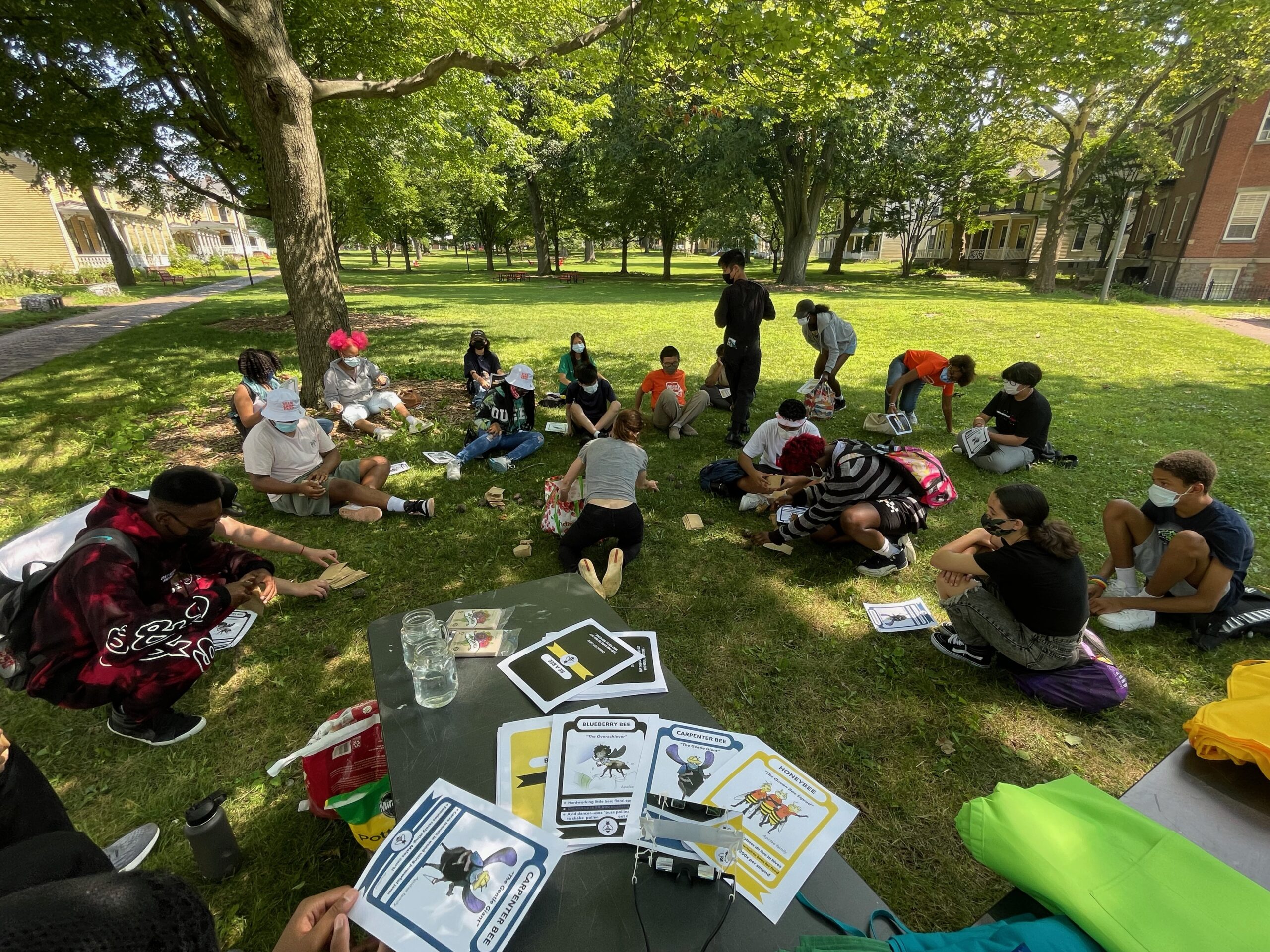 Group of students sit in a semi-circle in the grass as they receive instruction on Governors Island