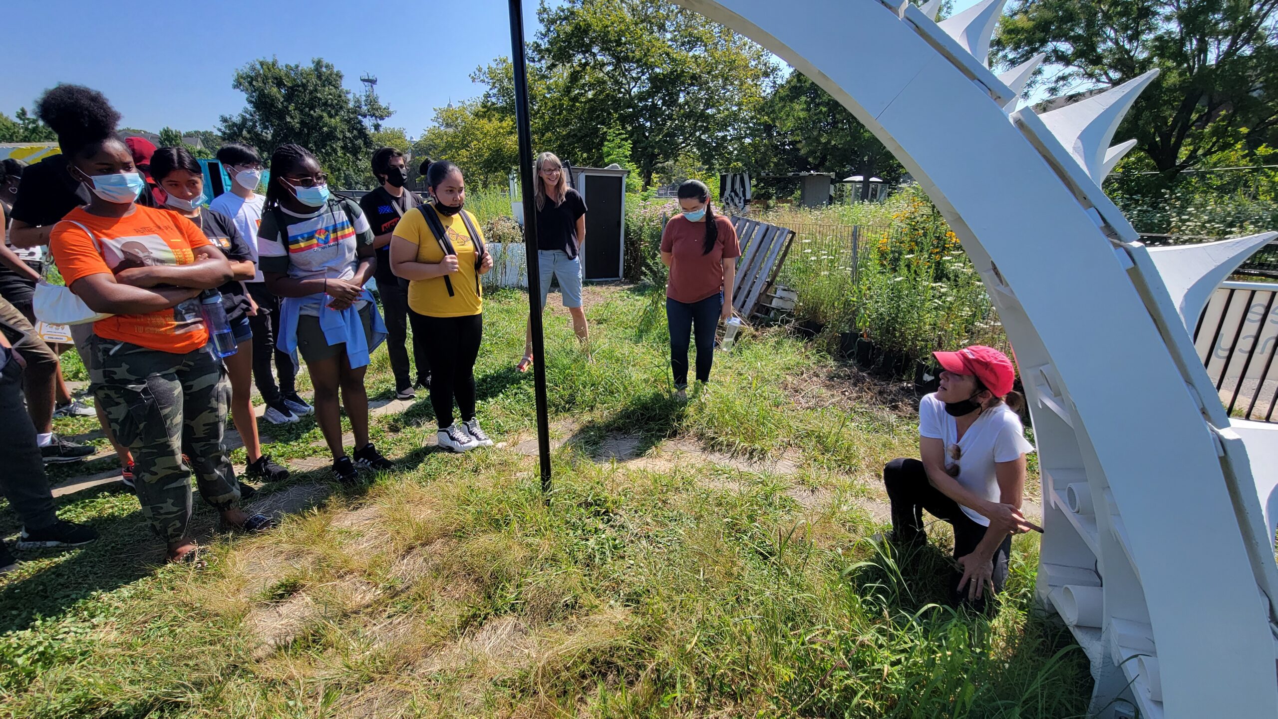 students stand in front of a "slice" of the Pollinators Pavilion as Ariane Harrison talks about the project.[