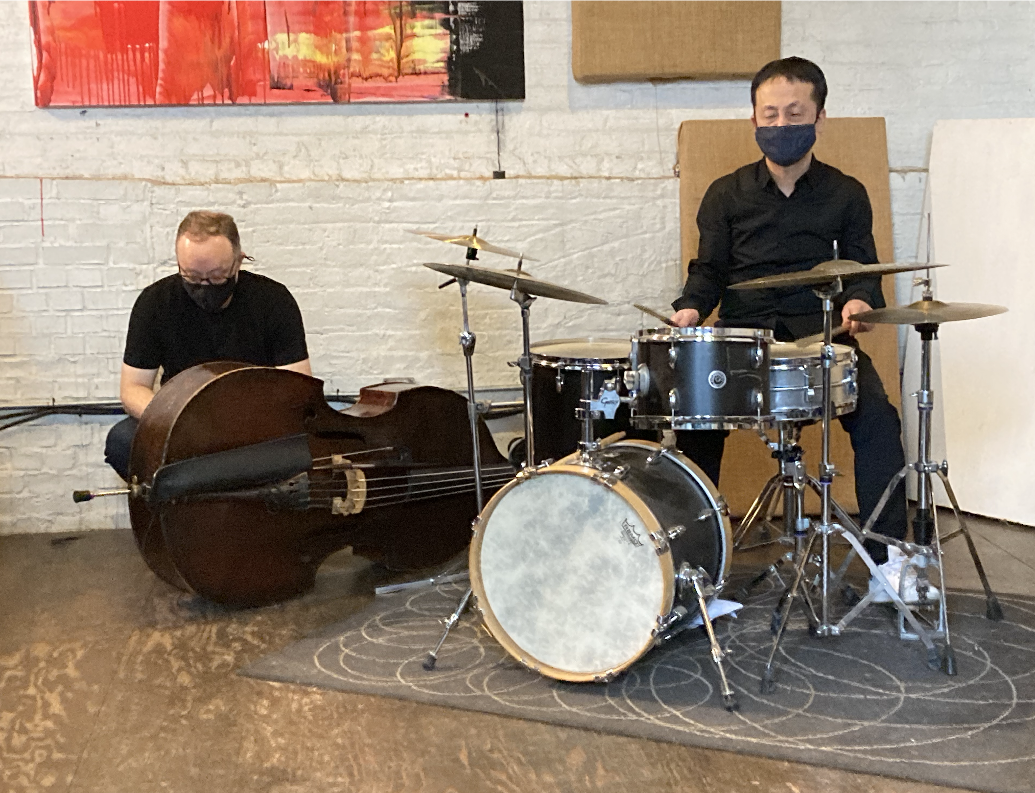 two musicians setting up their instruments for a performance, one is near an upright bass and the other is behind a drum set