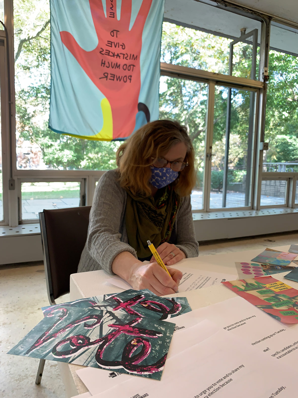 A masked person writes postcards in DeKalb Gallery at Pratt Institute