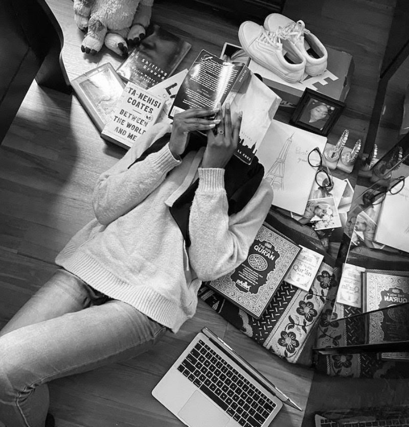 Teenage girl has book over her face, surrounded by objects that are tied to her identity