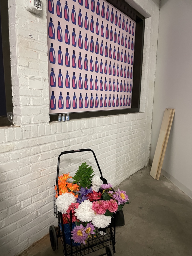 grocery cart with flowers in front of a pattern of printed laundry detergent bottles