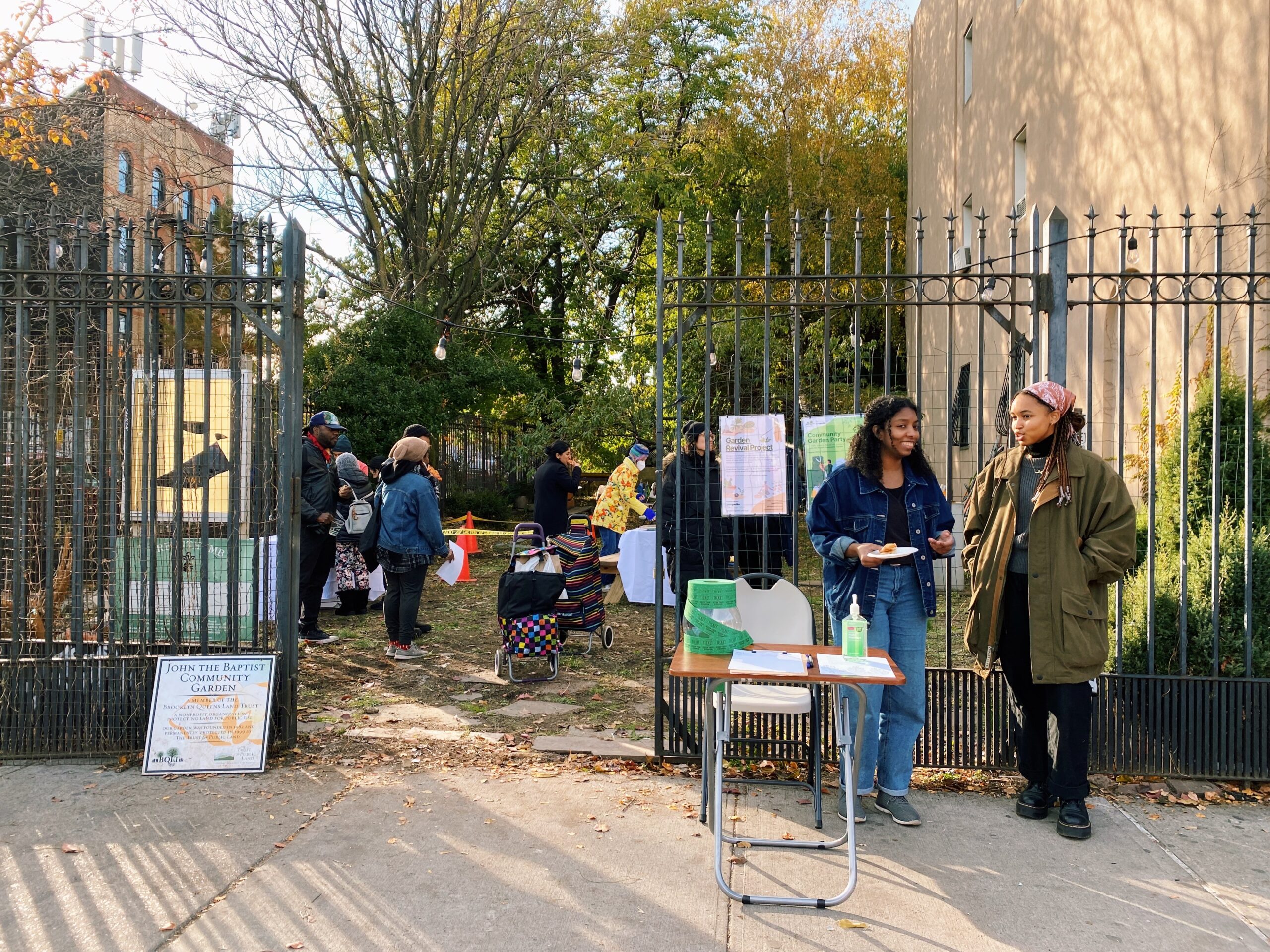 two people stand outside of the opened gate of John the Baptist Garden with others congregating inside.