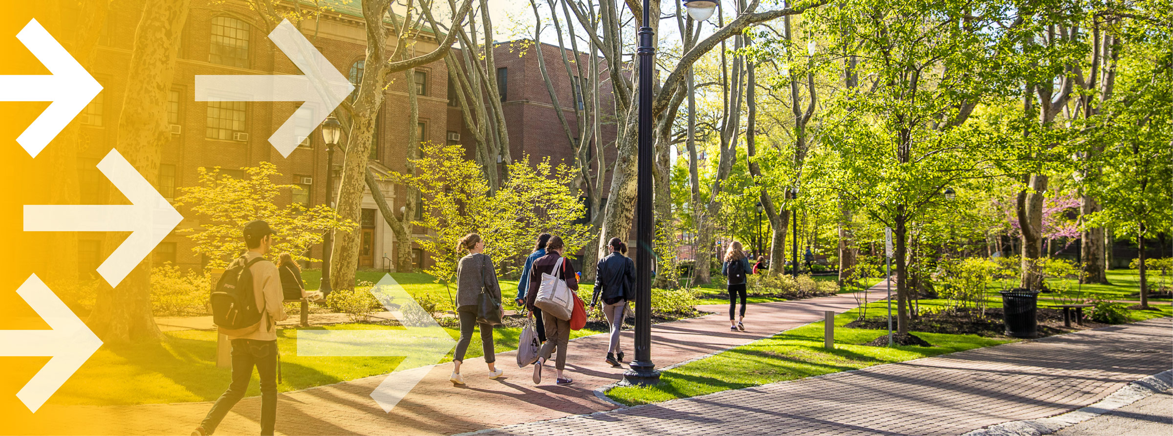 Students walk along a path on campus. There are graphics of arrows pointing to right to signify motion.