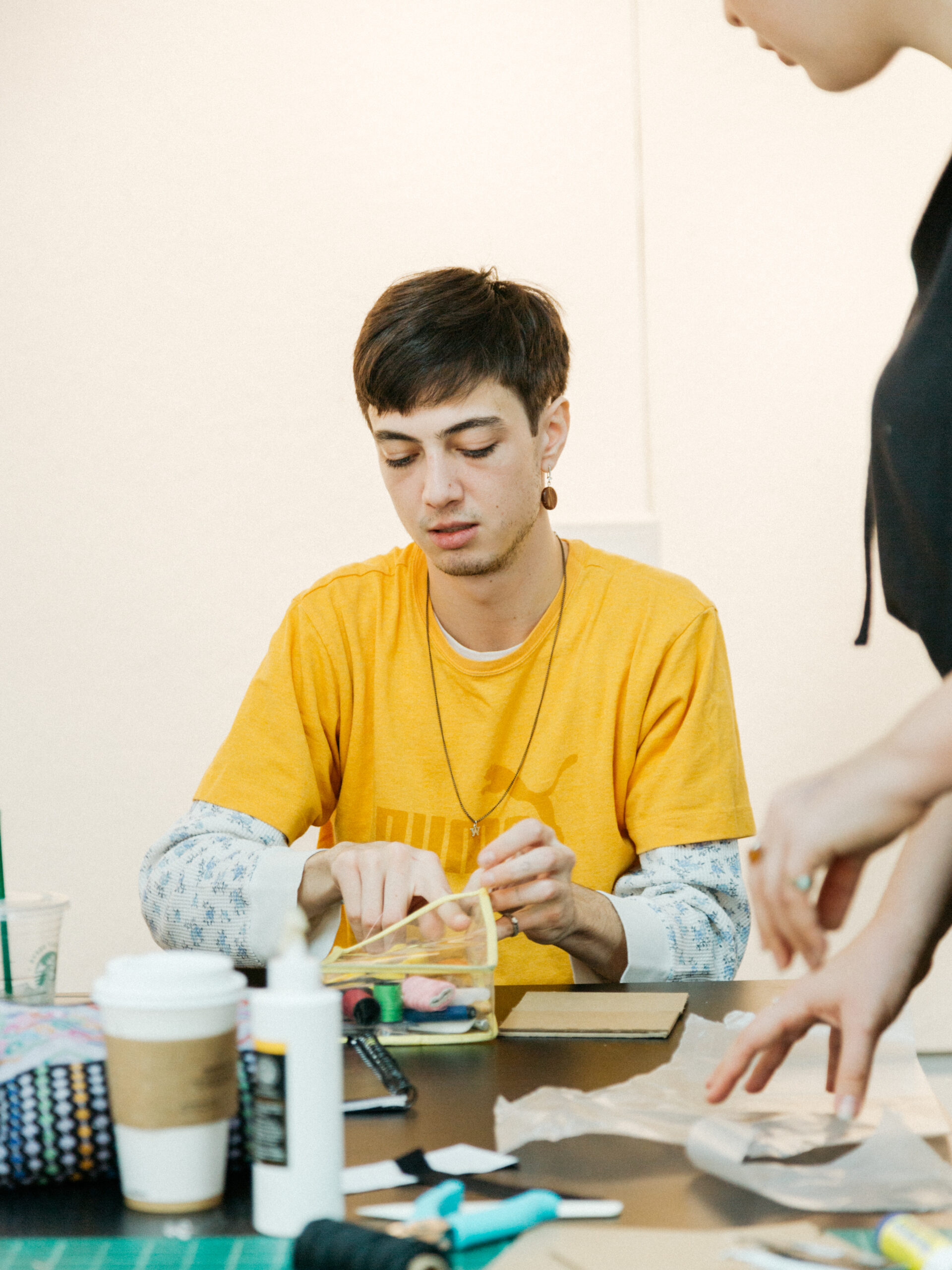 student cutting paper in background, at table with other student in foreground