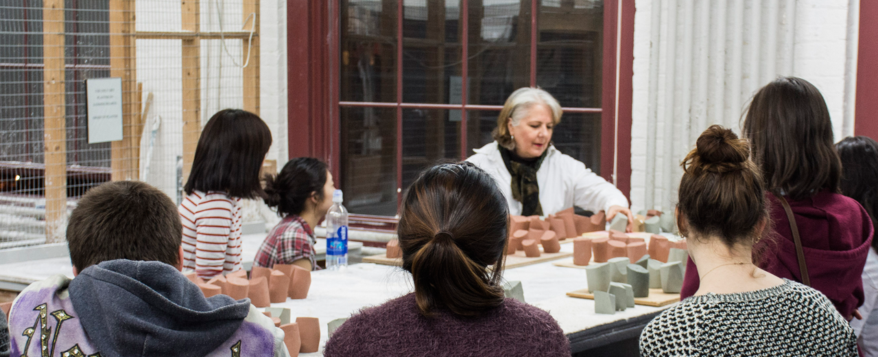 Students listen to their professor discuss sculptures laid out in front of her.