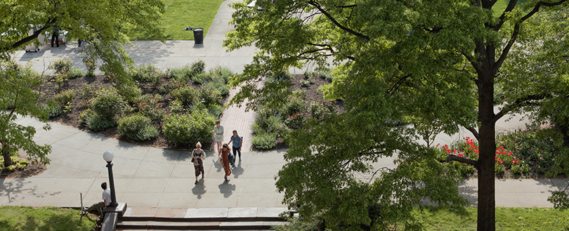 Aerial image of Pratt's campus quad. Student walk across a park, walking on a path surrounded by foliage.