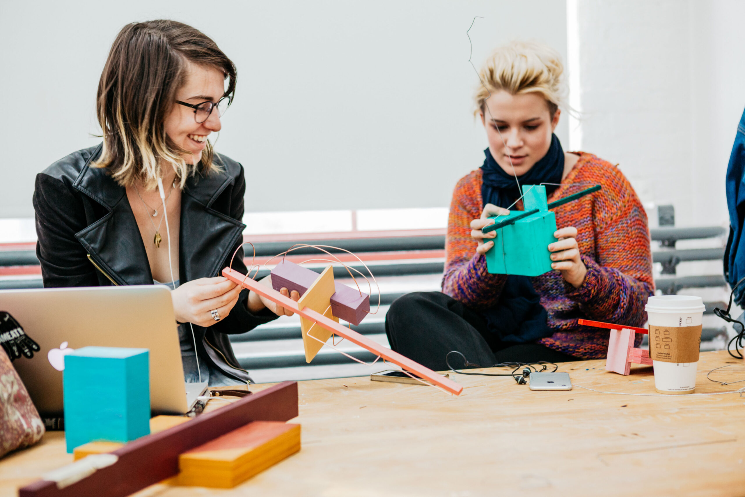 two students at a table, working with parts of a sculpture