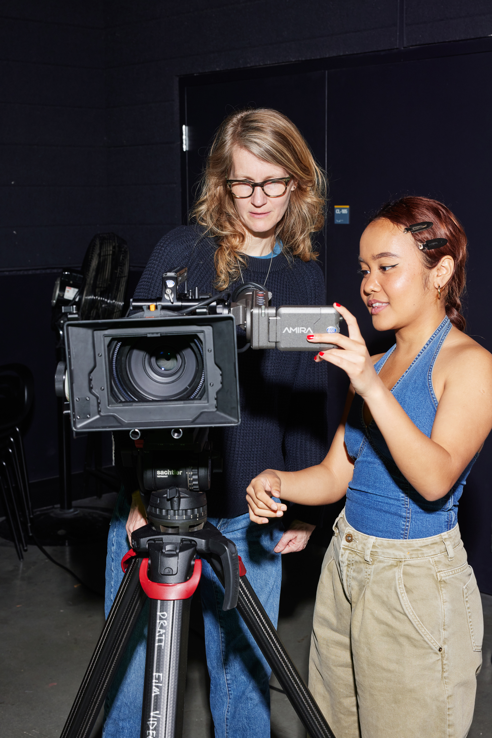 A photograph of a student looking at a video camera. A faculty member is giving guidance.