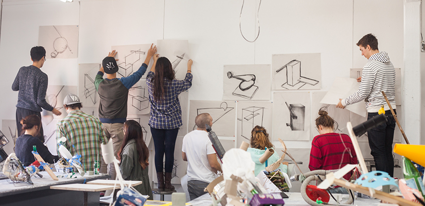 A group of students hangs their work on a wall within an art classroom.