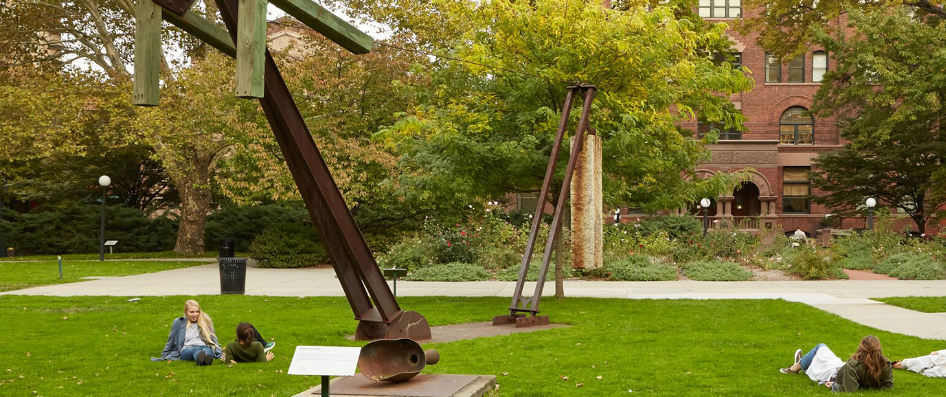 Students lay on the grass around the sculptures of Pratt's Sculpture Park.