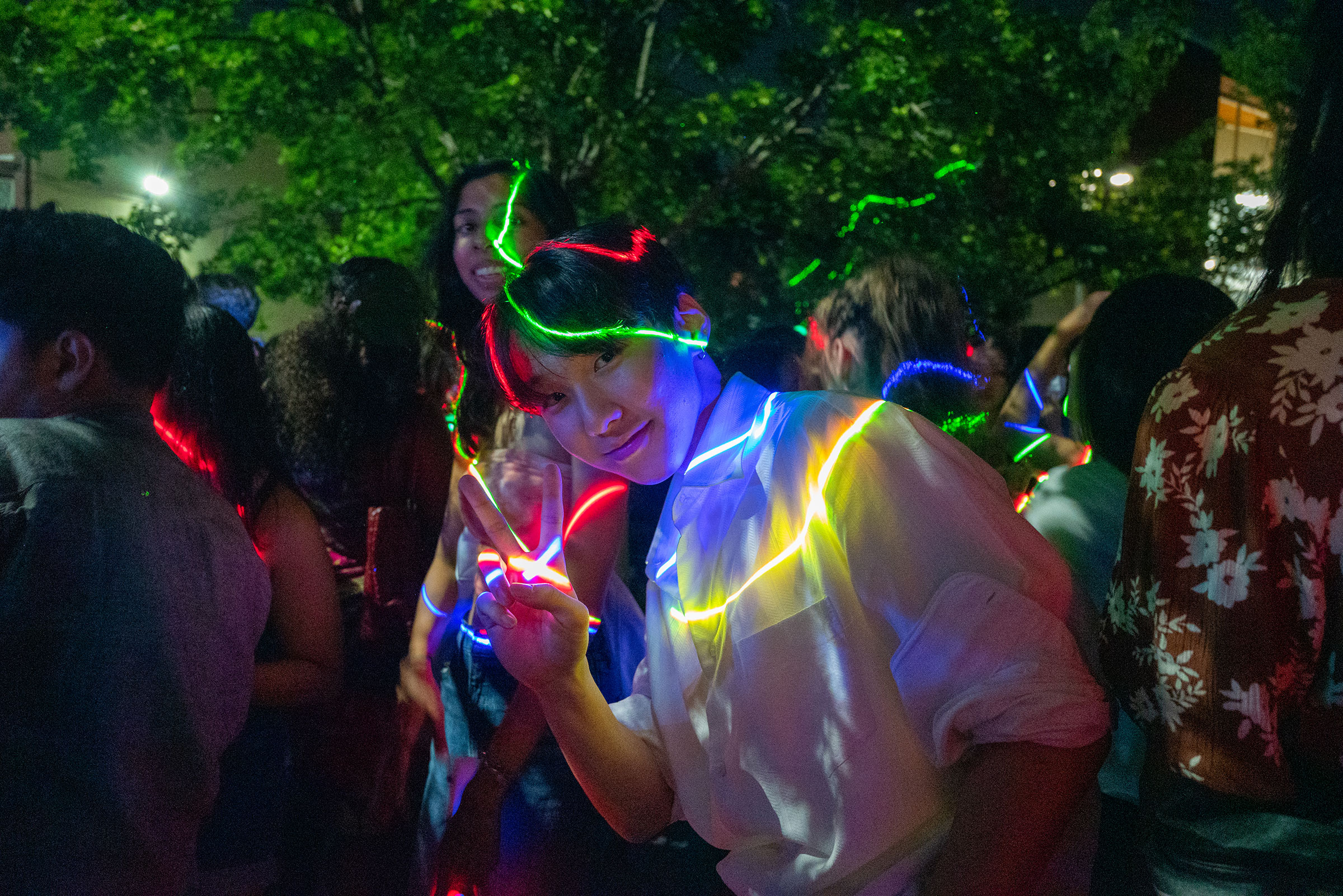 a college student giving the peace sign at the camera while glowing lights glow around him.  They're out on campus, it's dark, and they're in a crowd of other students