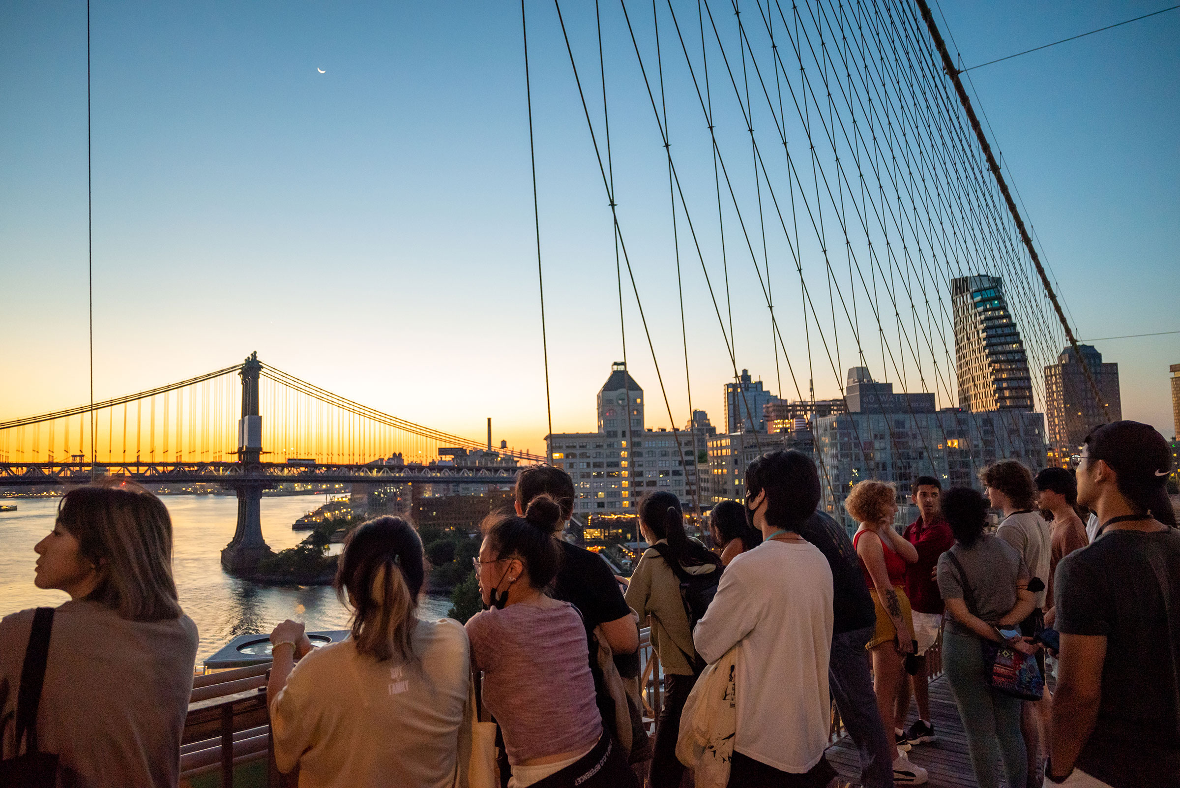 students look out from the Brooklyn Bridge as the sun rises over Brooklyn.